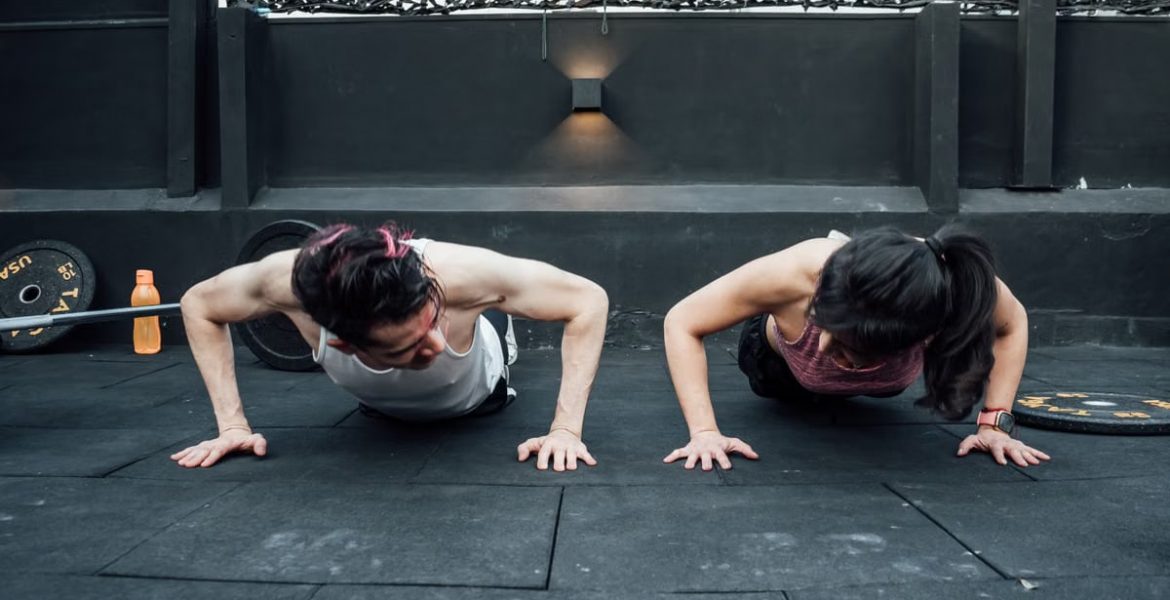 Two adults doing push-ups in an indoor gym setting in Mexico City, promoting a fit and healthy lifestyle.